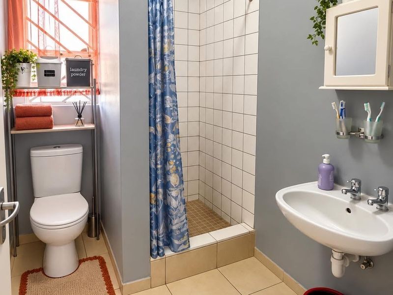 A functional bathroom featuring a tiled shower enclosure, a wall-mounted basin with chrome fixtures, and a standard toilet.