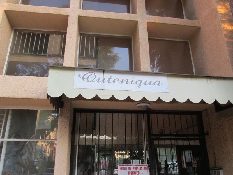 The front entrance of the Outeniqua apartment building, featuring a security gate, protective awning, and building signage.