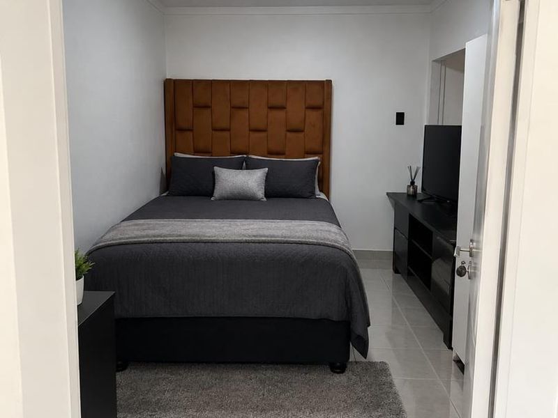 A compact bedroom featuring neutral tiled flooring and a modern flush mount ceiling light, presented in a clean and well-maintained condition.