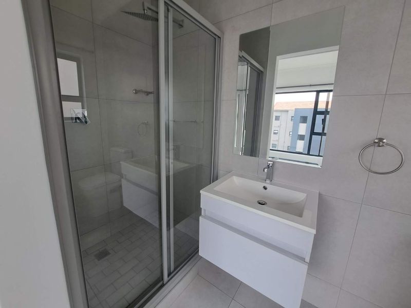 Modern bathroom featuring a wall-mounted vanity, glass shower enclosure with rain shower head, and neutral floor-to-ceiling tiling.