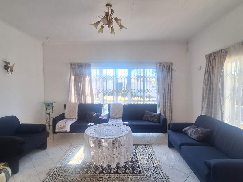 A bright living room featuring tiled flooring, security gates on windows, and classic lighting fixtures, offering a functional and well-lit space.