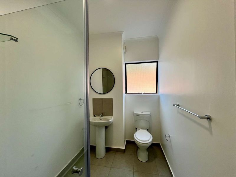 A clean and functional bathroom featuring a pedestal sink, toilet, and a glass-enclosed shower with neutral floor tiling.