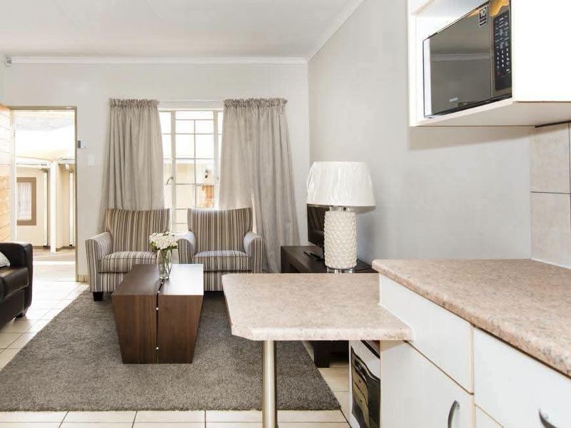 Open-plan living area featuring a compact kitchen with built-in cabinetry and microwave, flowing into a comfortable lounge space with direct outdoor access.
