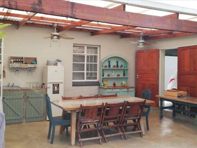 Covered outdoor patio area featuring a timber pergola, ceiling fans, built-in cabinetry with a sink, and concrete flooring, ideal for alfresco dining.