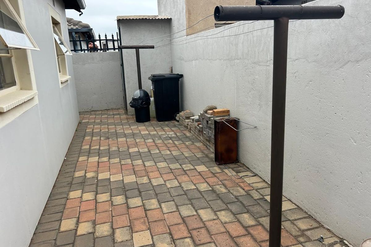 A paved side yard area featuring a metal washing line, enclosed by perimeter boundary walls.