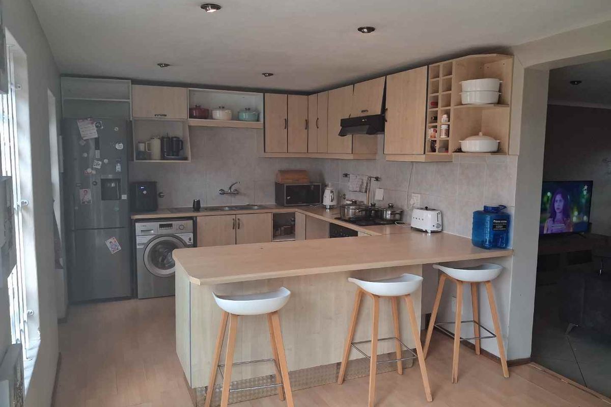A functional kitchen featuring light wood-finish cabinetry, a breakfast bar, integrated sink, and built-in extractor fan, with an adjacent laundry area.