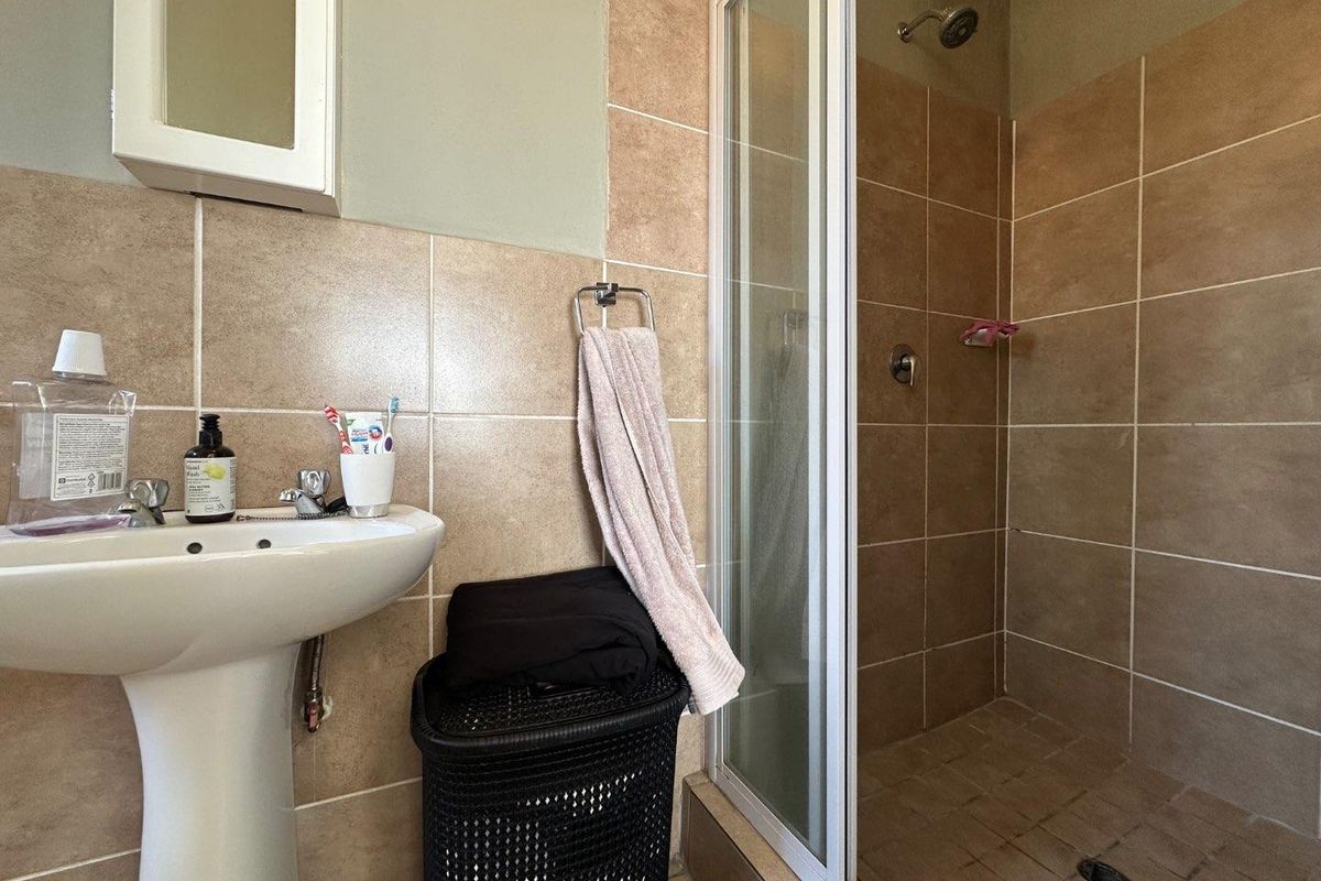 A functional bathroom featuring a pedestal basin, a shower enclosure with tiled walls, and a medicine cabinet, presenting a dated but practical layout.