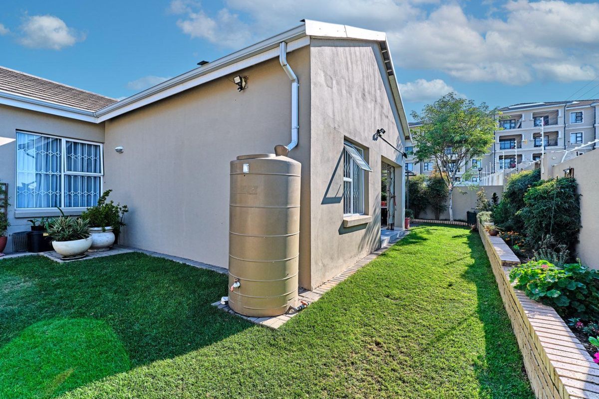 Rear exterior view of the property featuring a well-maintained lawn, brick retaining wall, and a functional water tank installation.