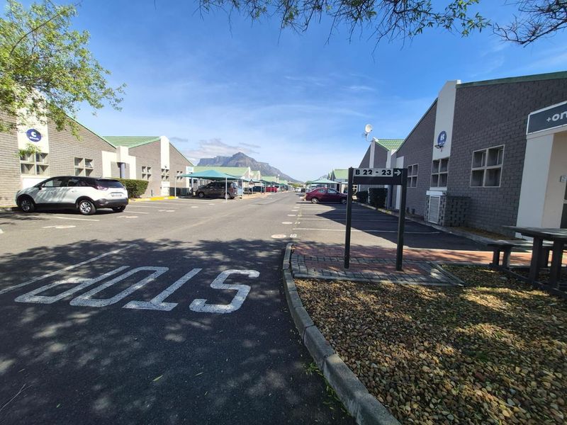 Exterior view of an office park complex featuring paved parking areas, covered bays, and well-maintained brick office buildings with mountain views.