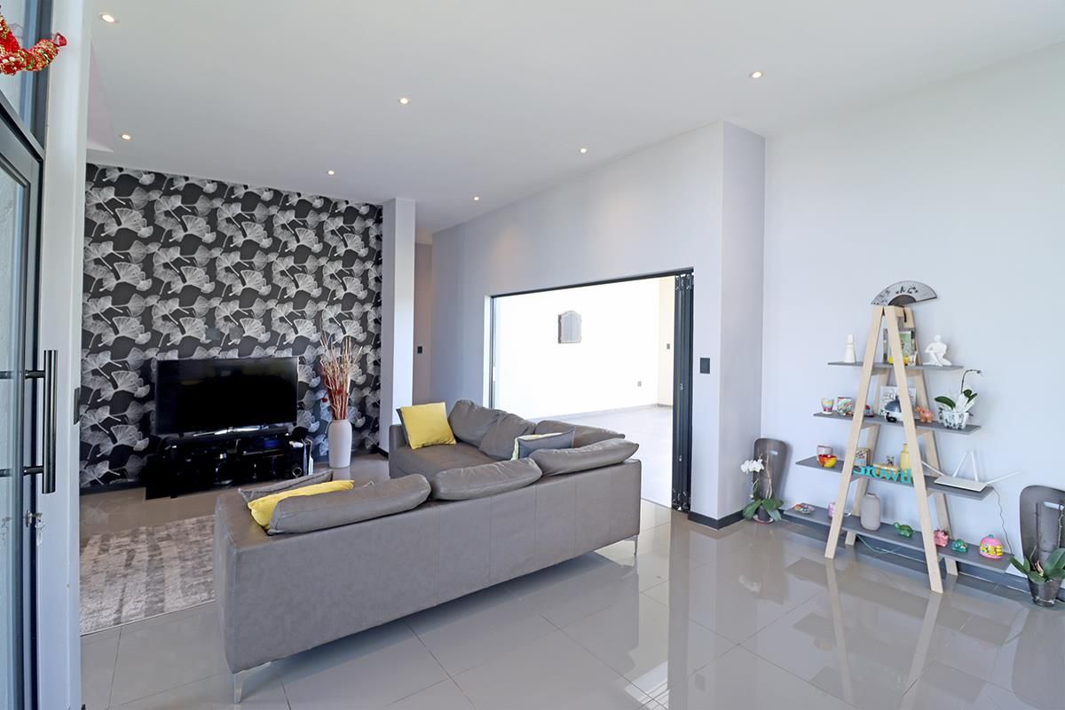 Modern living room featuring large format floor tiles, recessed downlighting, and a striking patterned feature wall, with seamless access to an adjacent room.