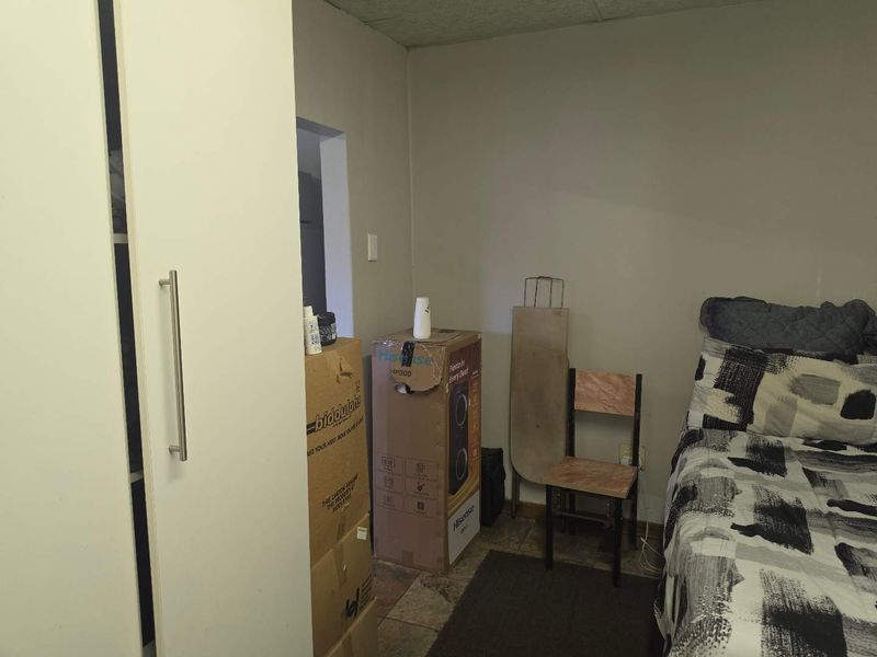 A bedroom featuring a built-in wardrobe and tiled flooring, currently cluttered with personal items and storage boxes.