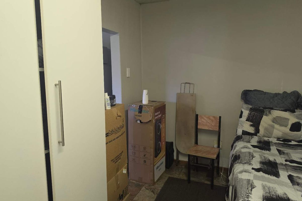 A bedroom featuring a built-in wardrobe and tiled flooring, currently cluttered with personal items and storage boxes.