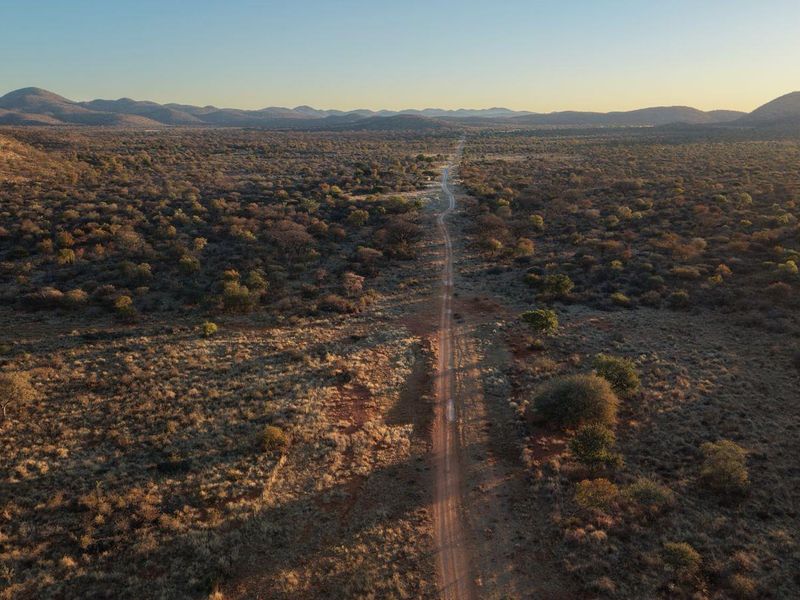 An expansive aerial view of the surrounding bushveld landscape, showcasing the vast natural terrain and access road leading to the lodge property.
