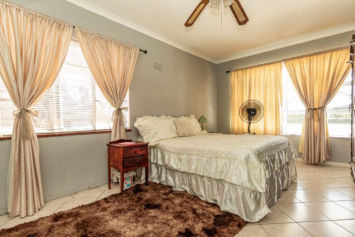 A bedroom featuring tiled flooring, ceiling fan, and dual windows with curtain treatments.