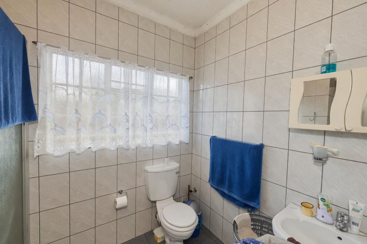 A functional bathroom featuring full-height wall tiling, a standard toilet, and a wall-mounted basin with a mirrored cabinet.