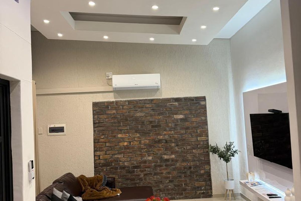Modern living room featuring a coffered ceiling with recessed lighting, an exposed brick feature wall, and a sleek floating media console.