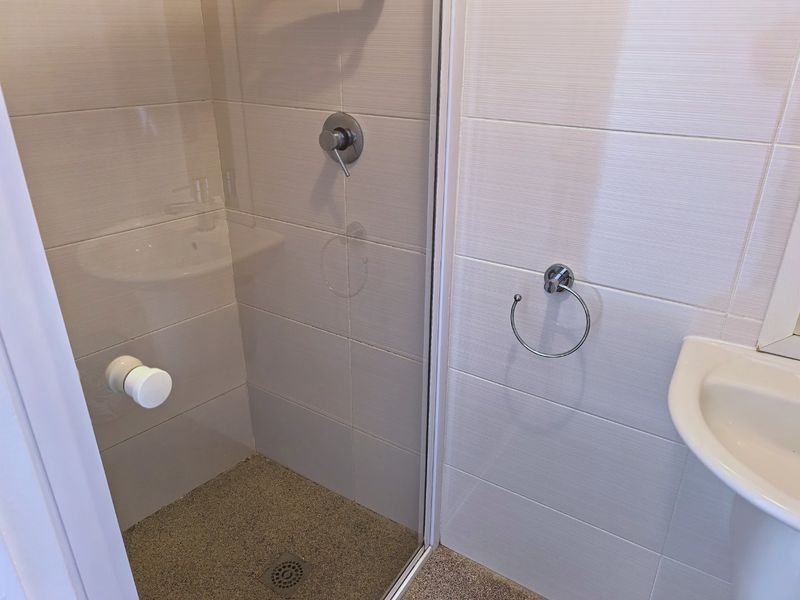 A clean, modern bathroom featuring a glass-enclosed shower, pedestal basin, and neutral wall tiling.