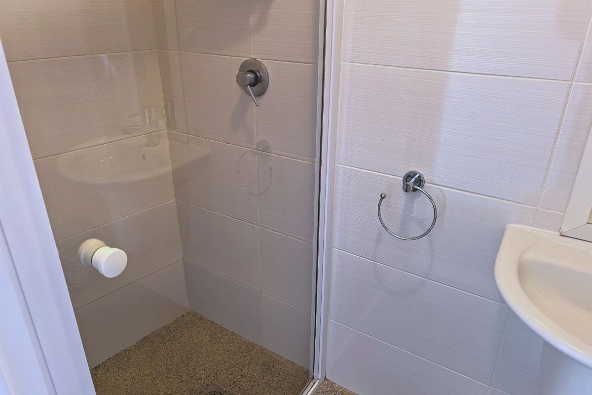 A clean, modern bathroom featuring a glass-enclosed shower, pedestal basin, and neutral wall tiling.