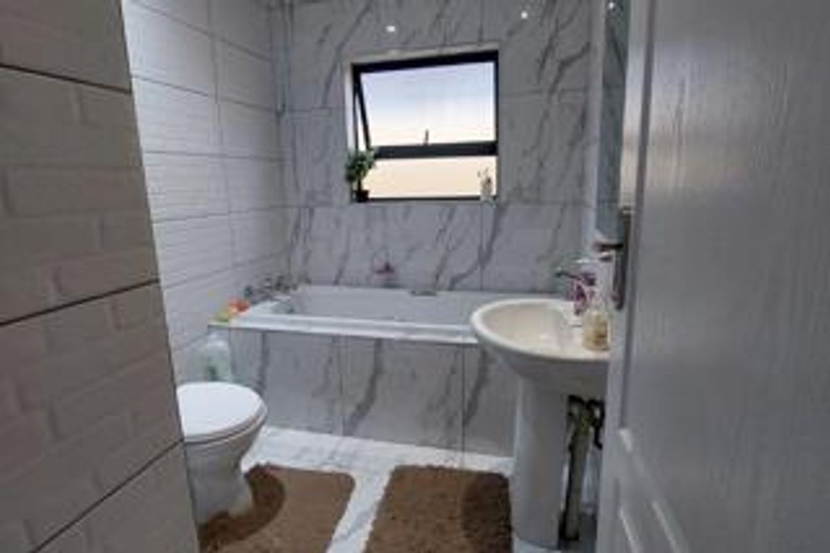 A modern bathroom featuring marble-effect wall and floor tiling, a built-in bathtub, and a pedestal sink.