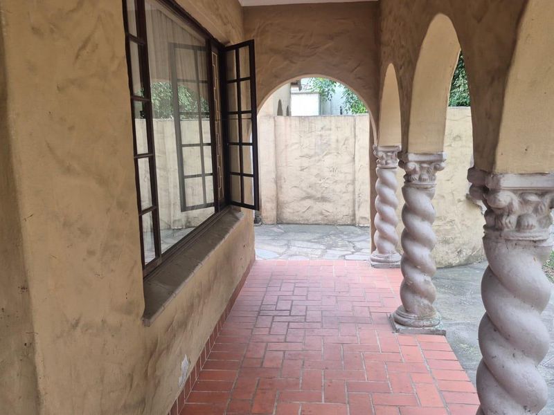 A covered patio area featuring distinctive spiral columns, terracotta tiled flooring, and textured stucco walls, providing a charming outdoor transition space.