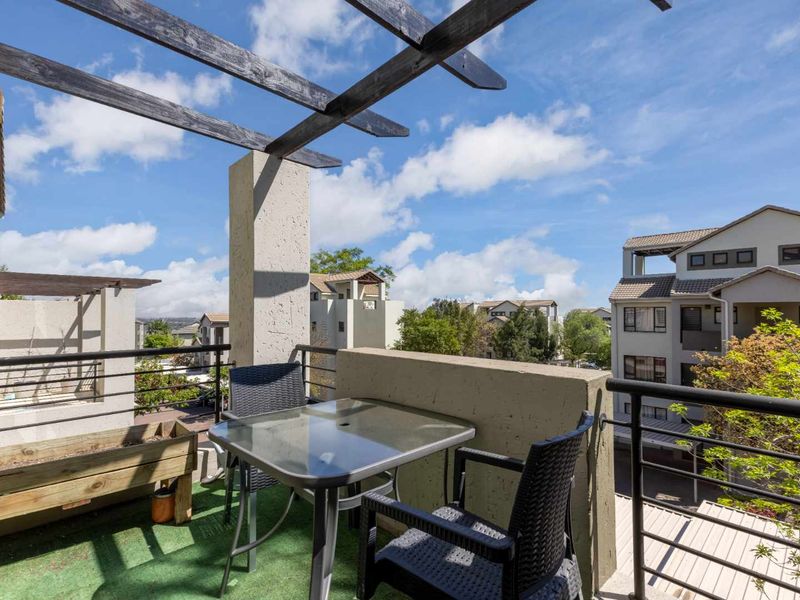 A private balcony featuring a timber pergola, metal balustrade, and concrete parapet wall, offering an open outdoor space with neighbourhood views.