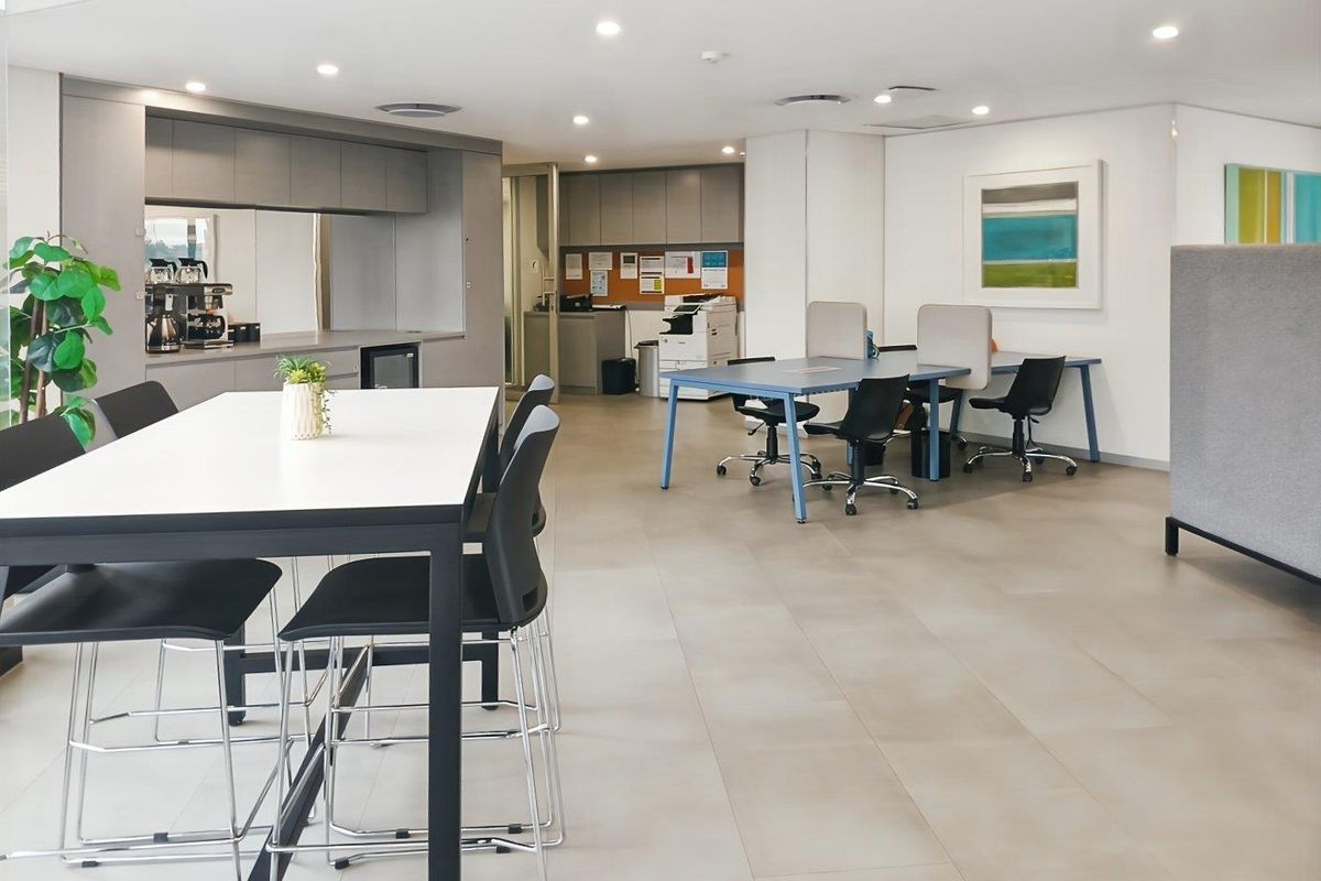A modern open-plan office space featuring a kitchenette area, tiled flooring, and recessed lighting, suitable for collaborative work environments.