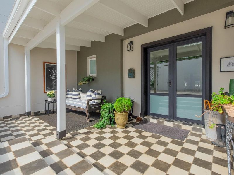 A well-maintained covered patio featuring classic checkered tile flooring and modern double glass doors, providing a stylish transition to the home's interior.