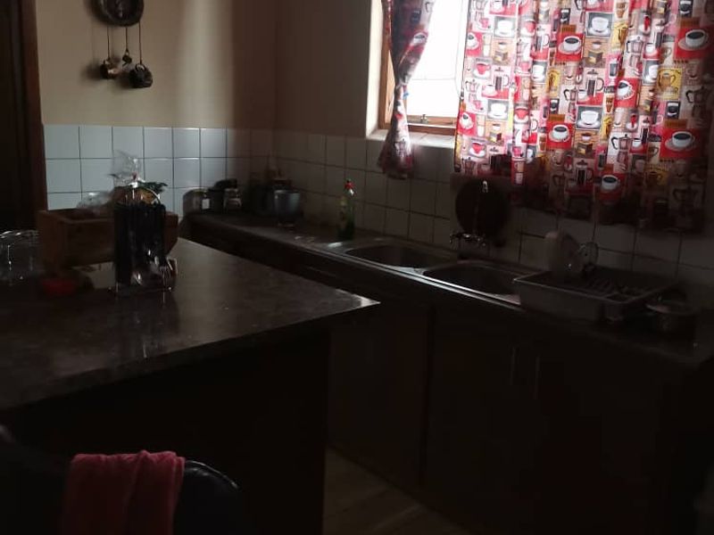 A functional kitchen featuring dark cabinetry, laminate countertops, a double stainless steel sink, and tiled backsplash with neutral wall finishes.