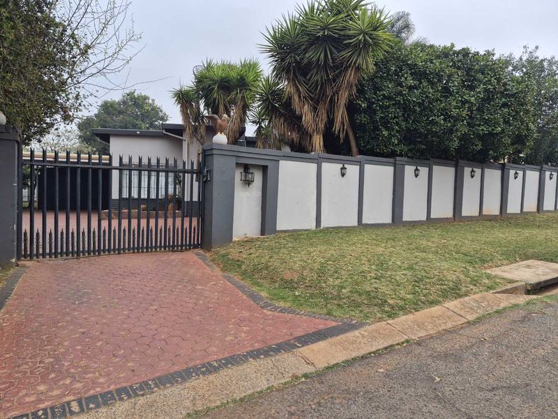 Front view of the property featuring a secure perimeter wall, metal driveway gate, and paved entrance area with established garden landscaping.