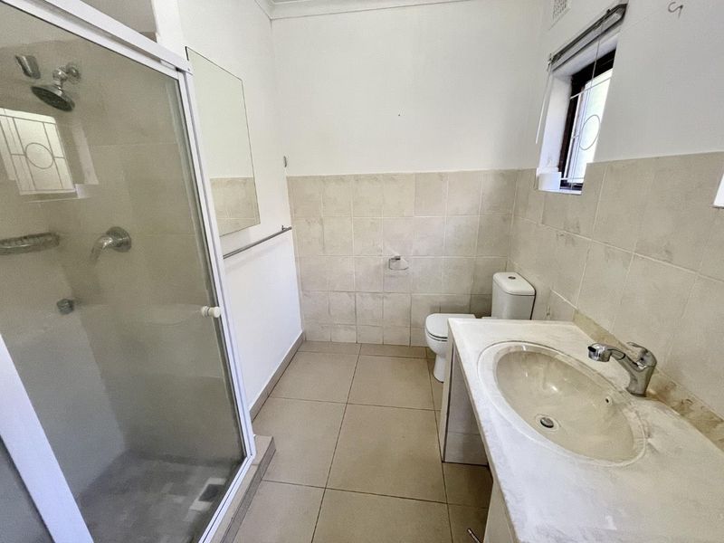 A functional bathroom featuring a shower enclosure, vanity basin, and toilet with neutral wall and floor tiling.