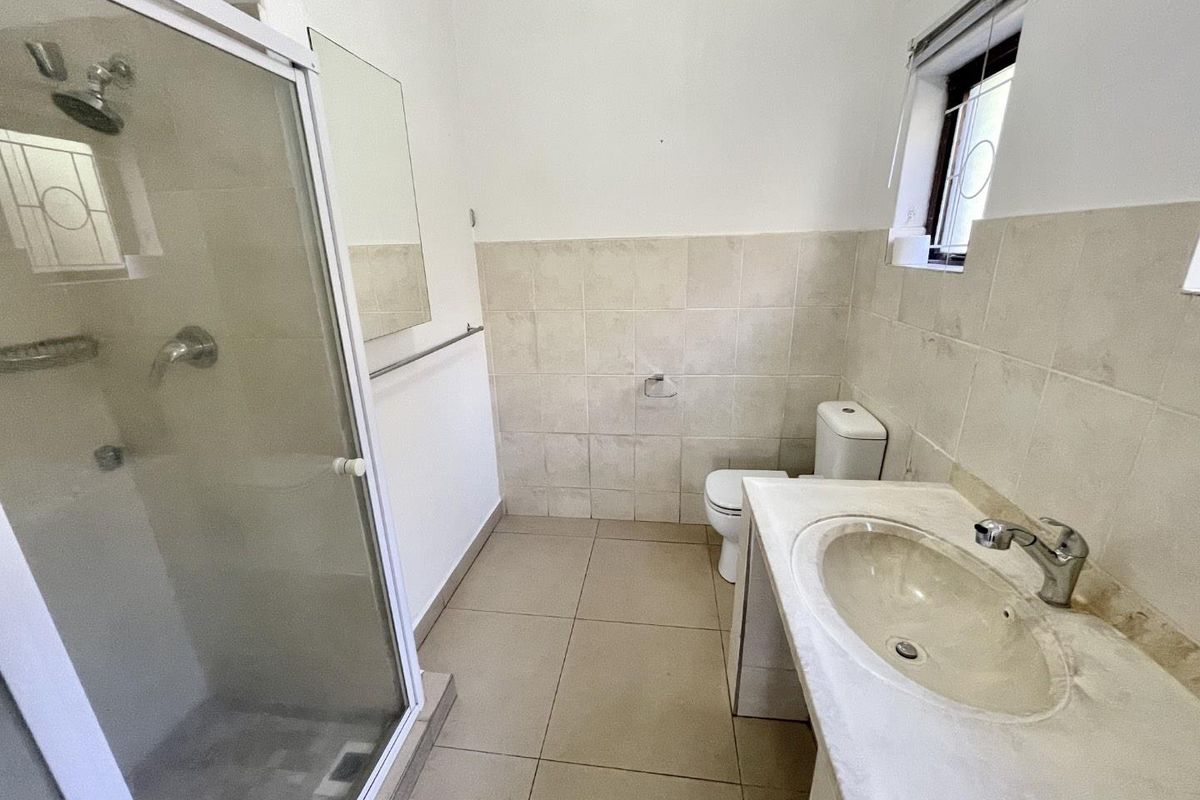 A functional bathroom featuring a shower enclosure, vanity basin, and toilet with neutral wall and floor tiling.