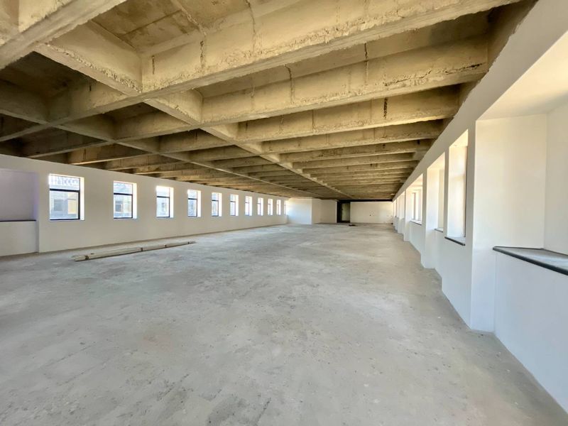 Spacious open-plan office area featuring an exposed concrete waffle ceiling, large windows providing natural light, and unfinished concrete flooring ready for customization.