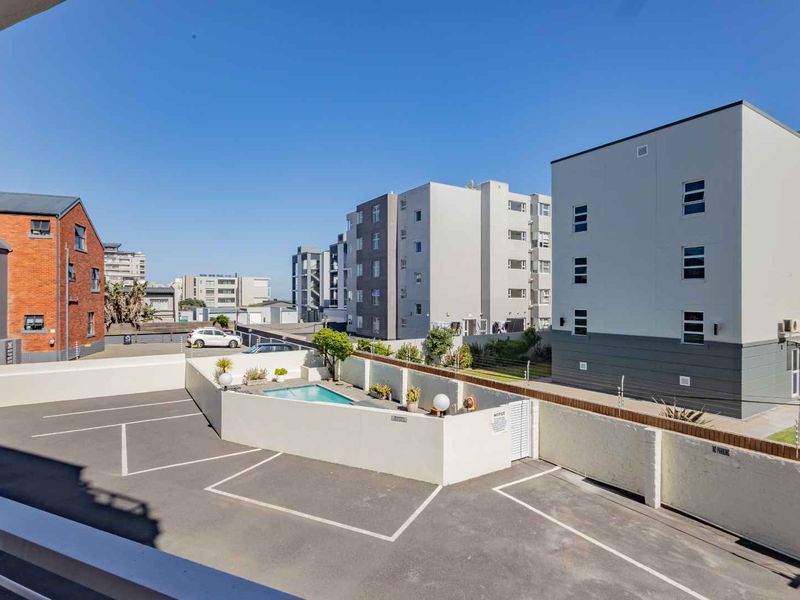 Elevated view overlooking a residential apartment complex featuring a communal swimming pool, paved parking area, and secure perimeter walling.