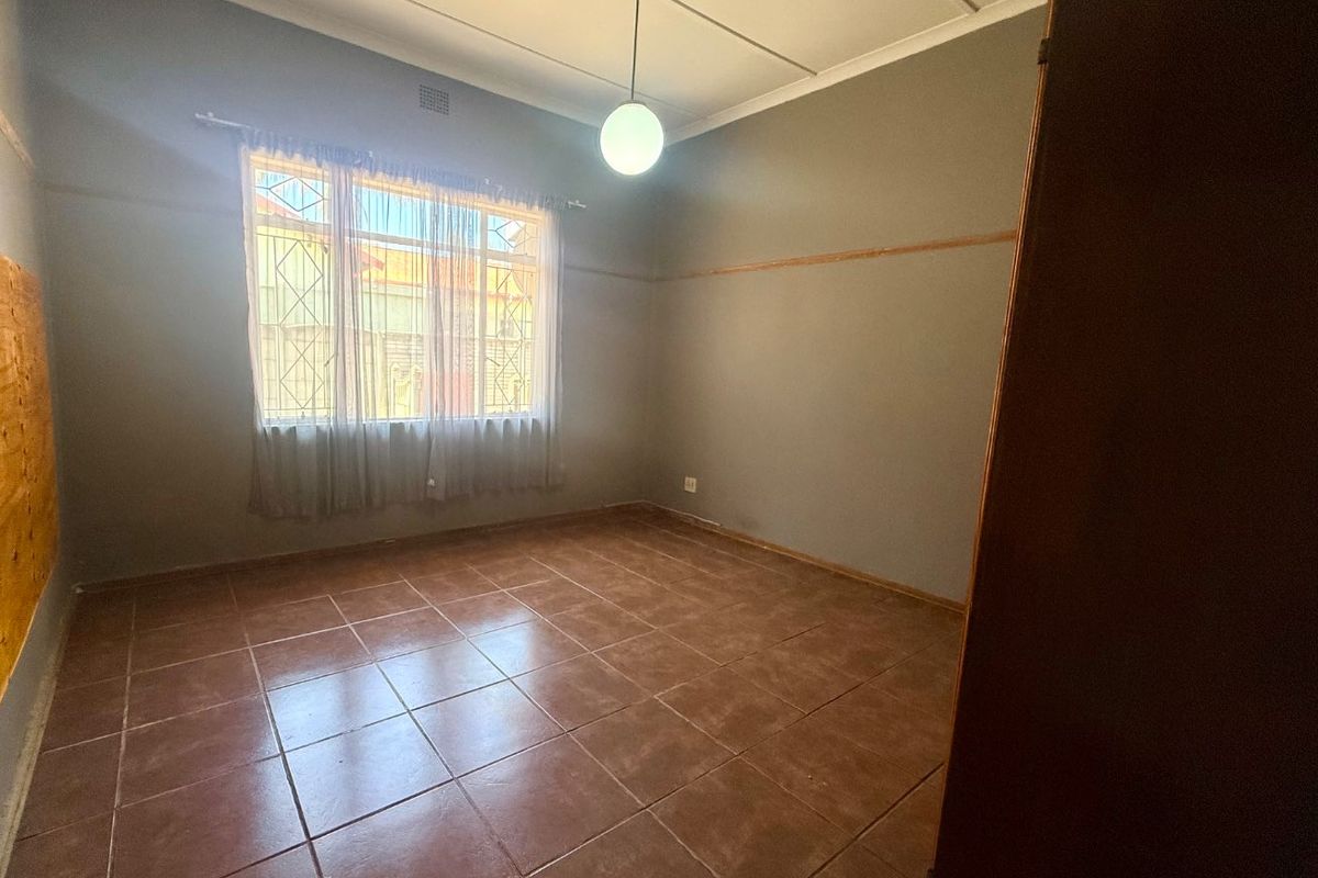 An empty bedroom featuring tiled flooring, a built-in cupboard, and security bars on the window, offering a blank canvas for renovation.