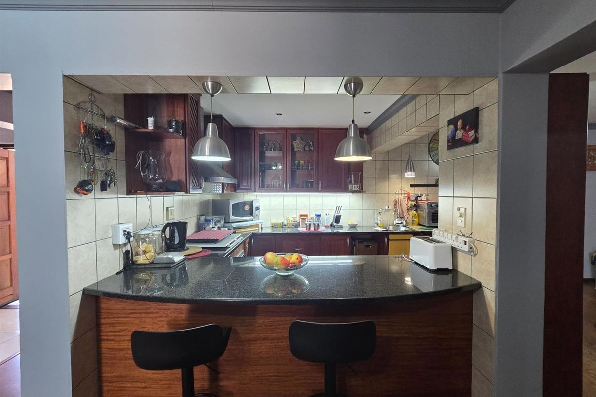 A functional kitchen featuring dark wood cabinetry, granite countertops, a breakfast bar, and tiled backsplash with integrated lighting.