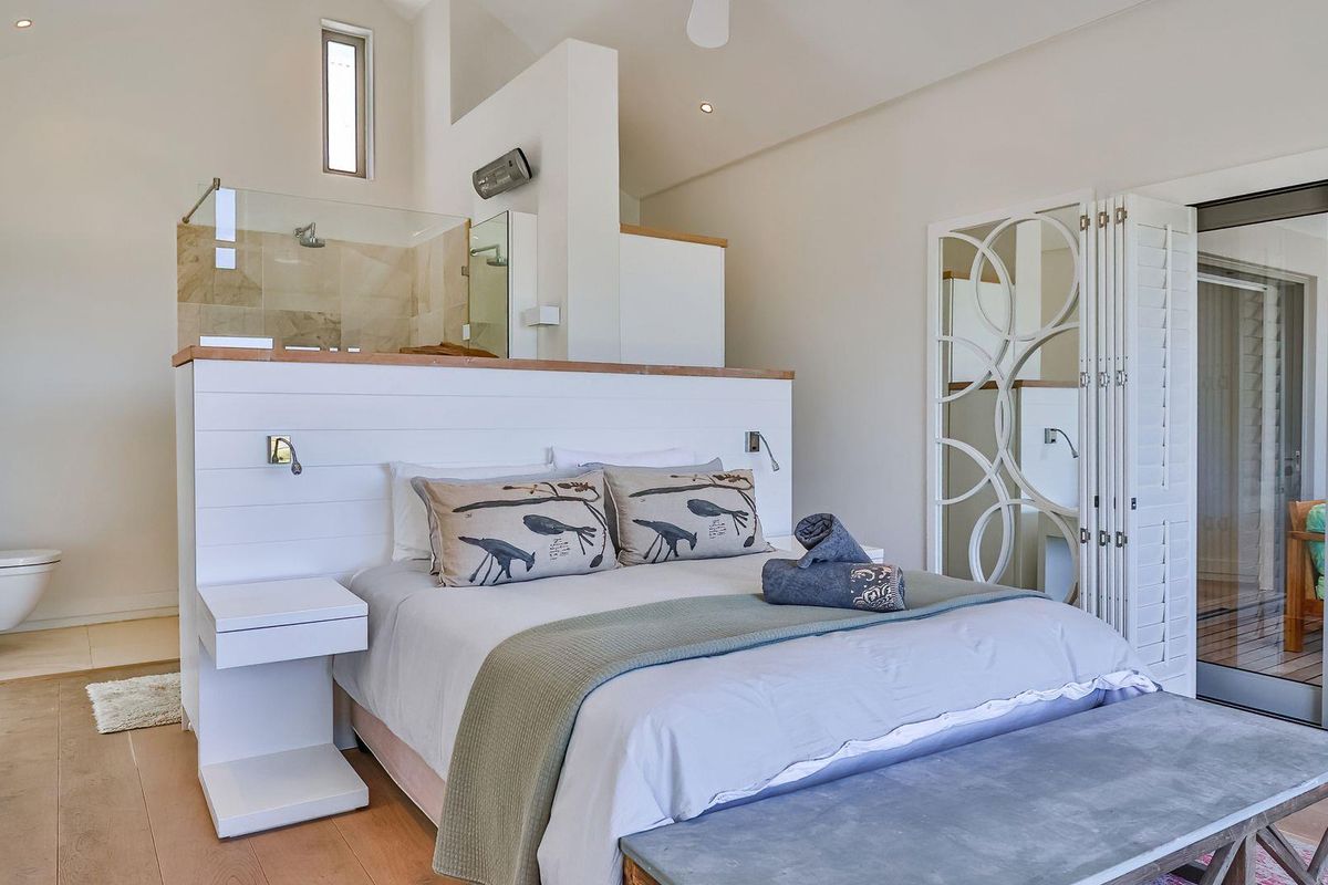 A modern open-plan bedroom featuring an integrated en-suite bathroom with a glass-enclosed shower and wall-mounted toilet, complemented by sliding doors to a private patio.