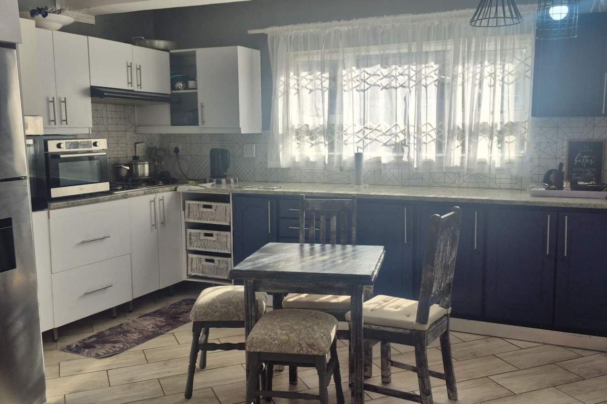 A functional kitchen featuring two-tone cabinetry, built-in oven, extractor fan, tiled backsplash, and durable laminate flooring with a dedicated breakfast nook area.