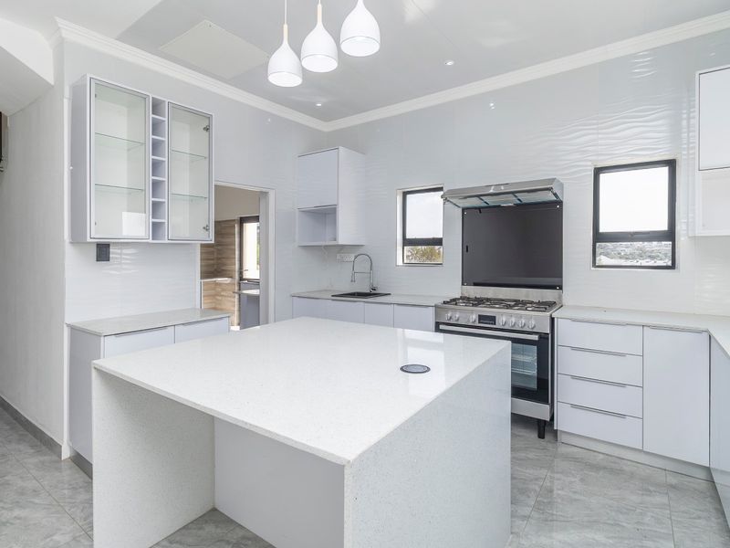 Modern kitchen featuring a central island with quartz countertops, gas stove, extractor fan, and sleek white cabinetry with textured wall tiling.