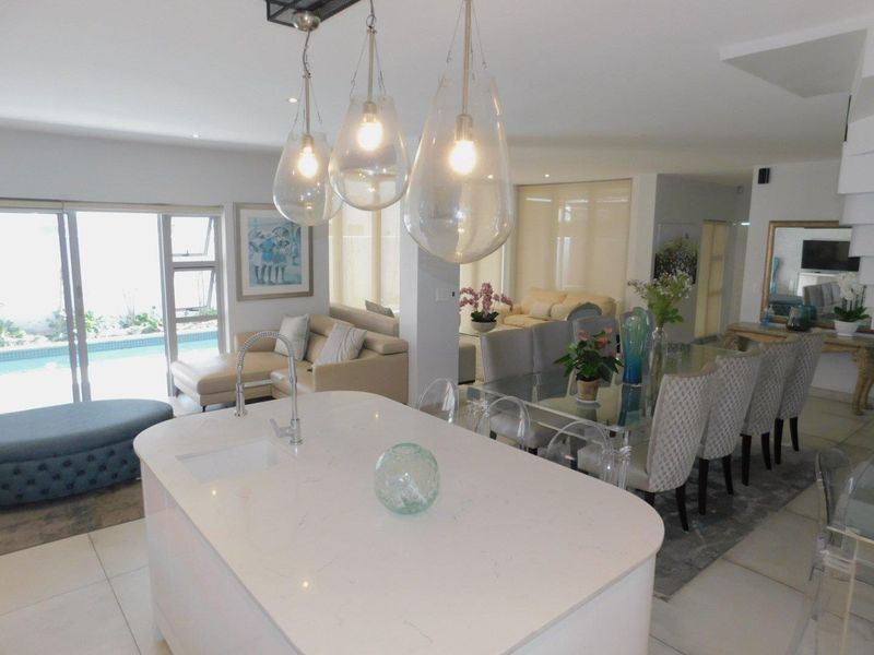 Spacious open-plan living area featuring a modern kitchen island with sink, contemporary pendant lighting, and seamless flow to the outdoor patio and pool area.