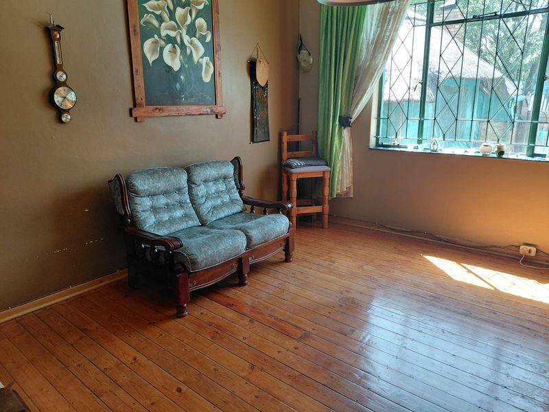 A living room featuring polished hardwood flooring and a large window with security bars, offering a classic, lived-in aesthetic.