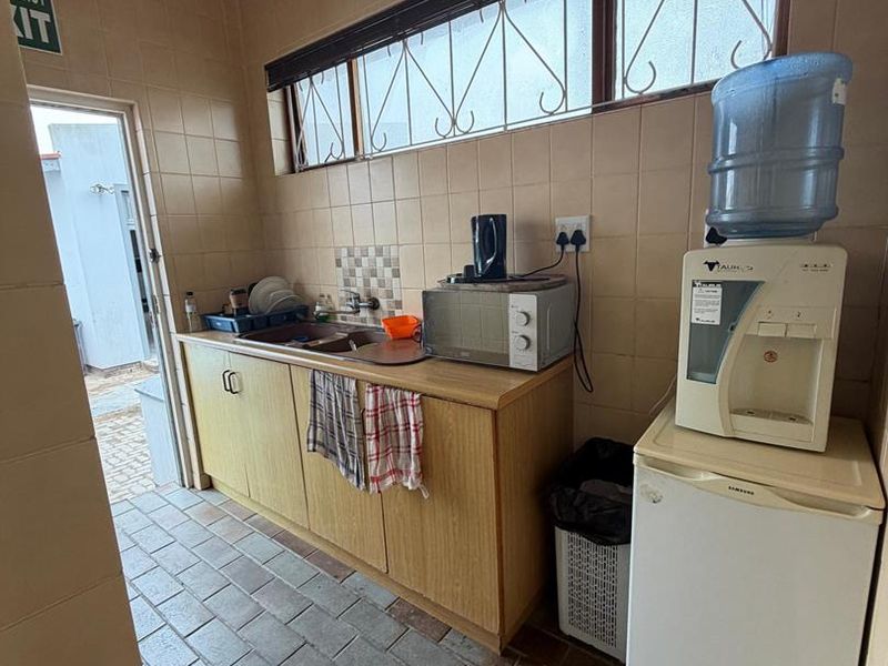 A functional office kitchenette featuring tiled walls and flooring, built-in cabinetry with a sink, and security bars on the windows.