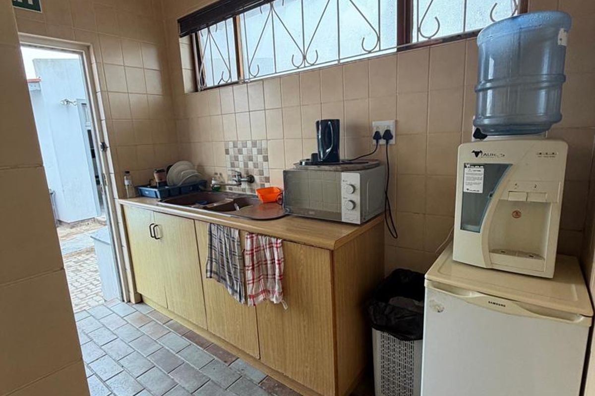 A functional office kitchenette featuring tiled walls and flooring, built-in cabinetry with a sink, and security bars on the windows.