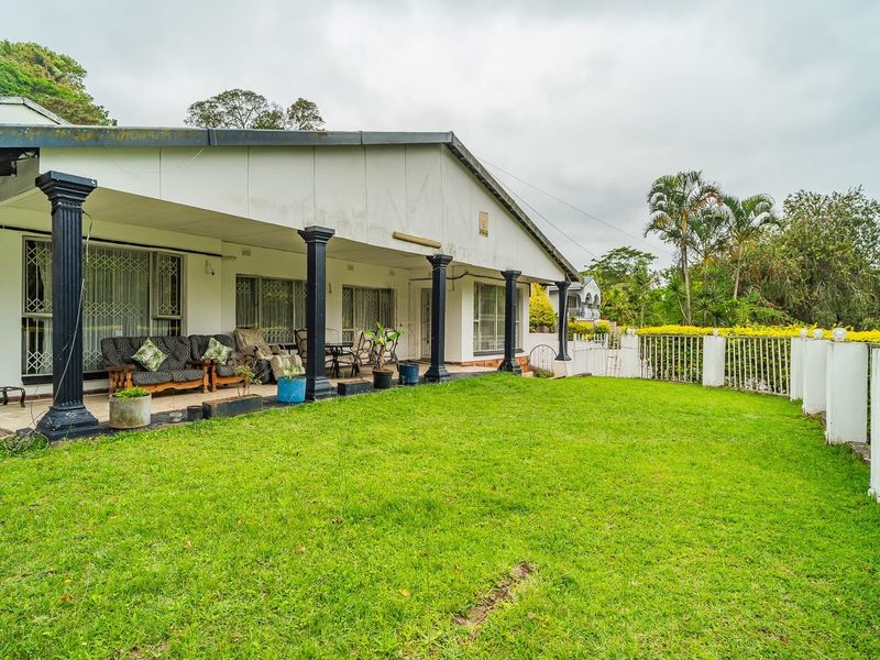 Spacious rear exterior featuring a covered patio with decorative columns, overlooking a well-maintained lawn and secure perimeter fencing.