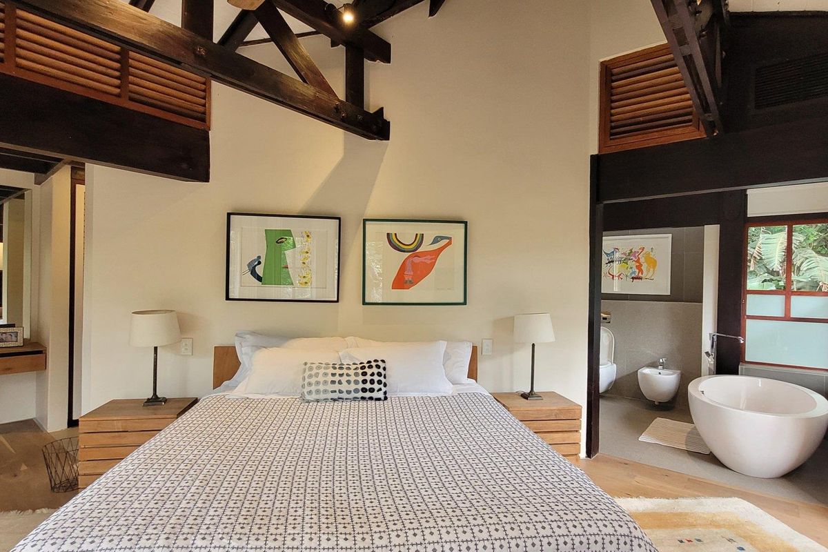 Spacious bedroom featuring exposed timber roof trusses, integrated ensuite bathroom with a freestanding soaking tub, and neutral finishes.