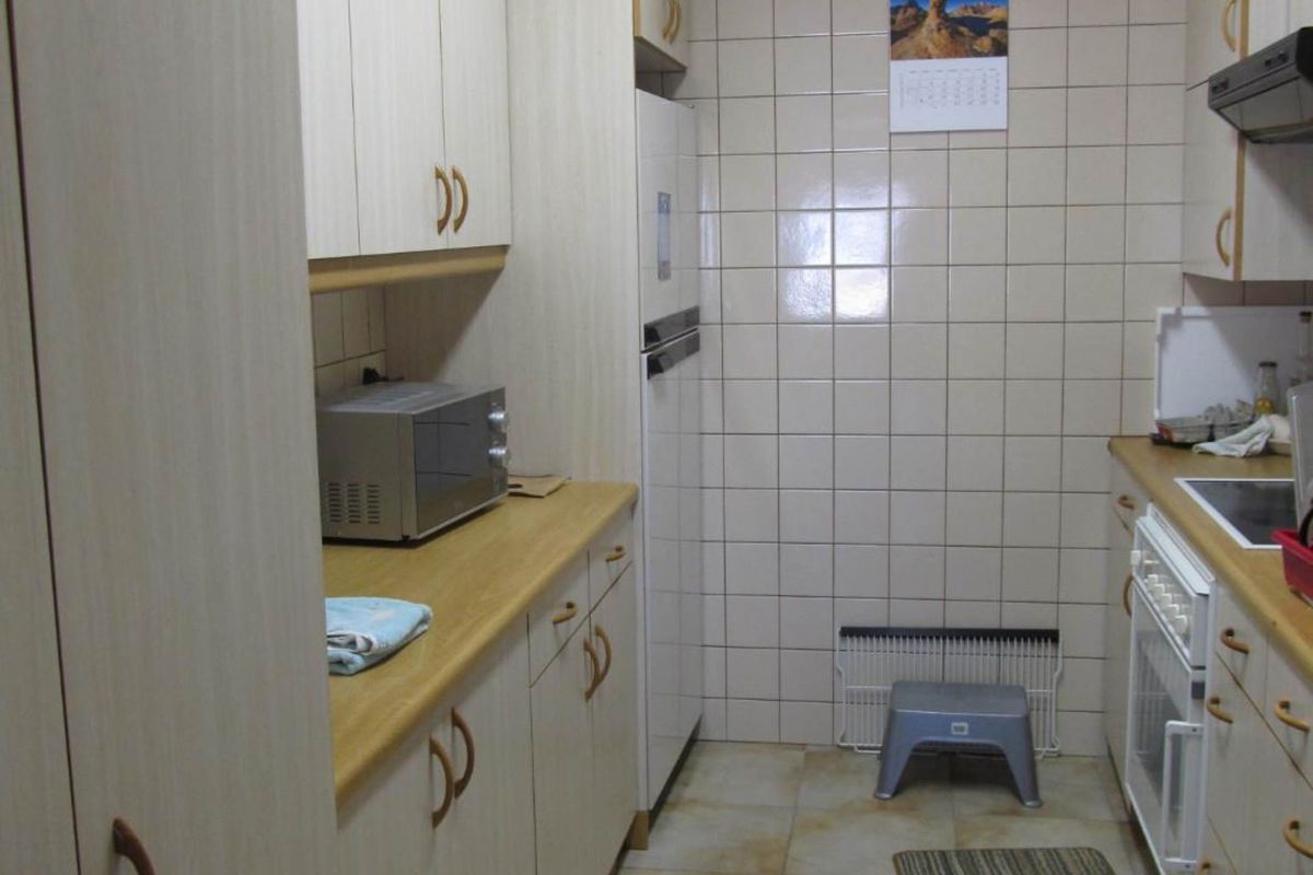 A functional galley-style kitchen featuring light-toned cabinetry, tiled walls, and integrated cooking appliances.