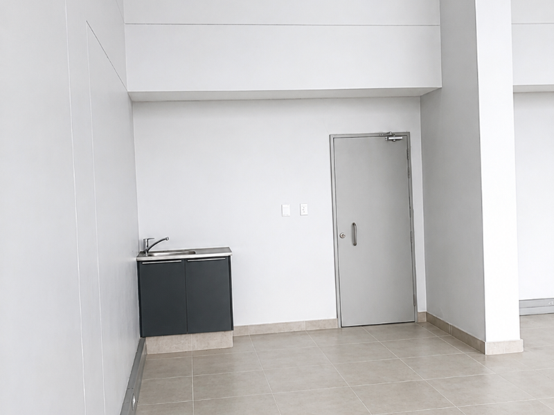 A clean, minimalist utility space featuring tiled flooring, a compact built-in kitchenette cabinet with a sink, and a secure metal door.