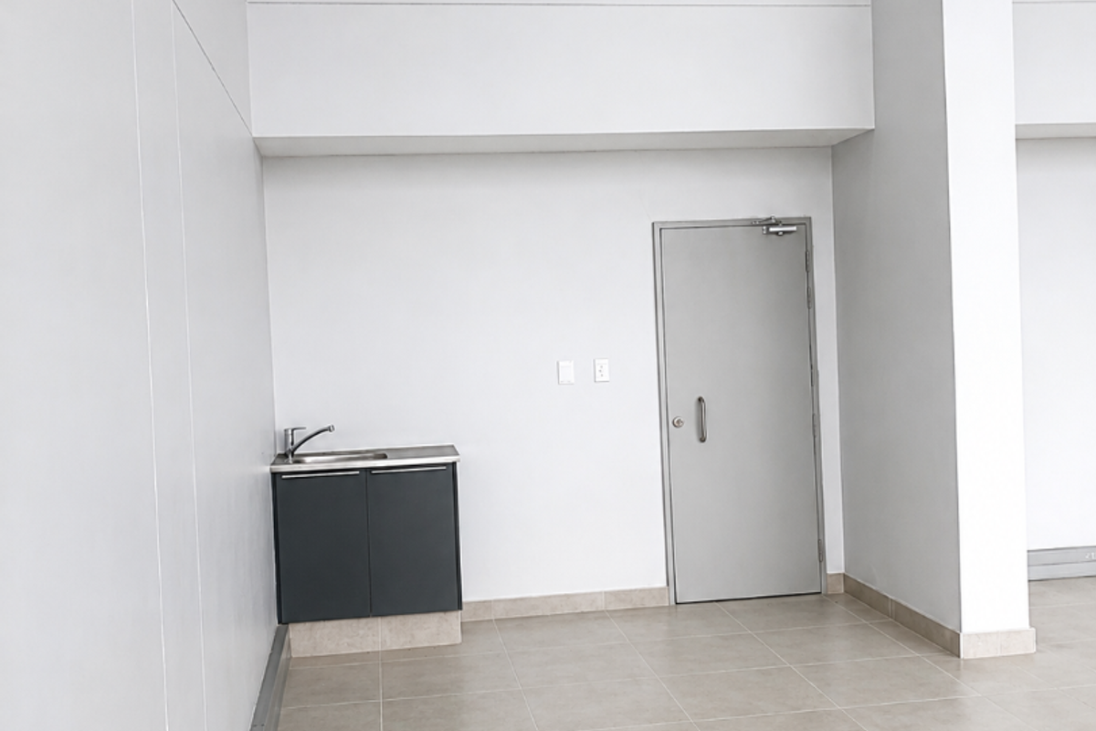 A clean, minimalist utility space featuring tiled flooring, a compact built-in kitchenette cabinet with a sink, and a secure metal door.