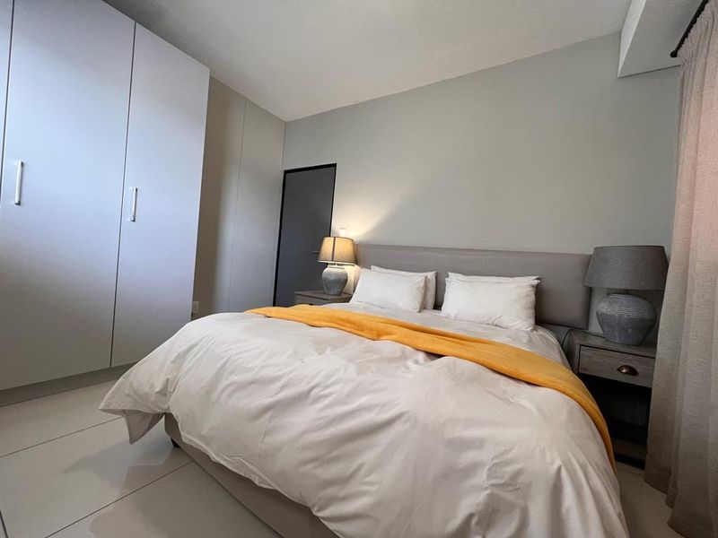 A well-maintained bedroom featuring neutral tones, built-in cupboards, and tiled flooring, creating a clean and comfortable living space.
