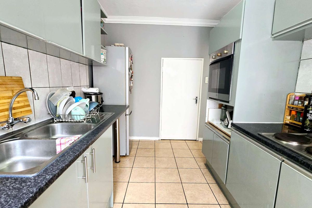 Functional galley-style kitchen featuring built-in cabinetry, integrated oven, hob, and double stainless steel sink with tiled splashbacks.
