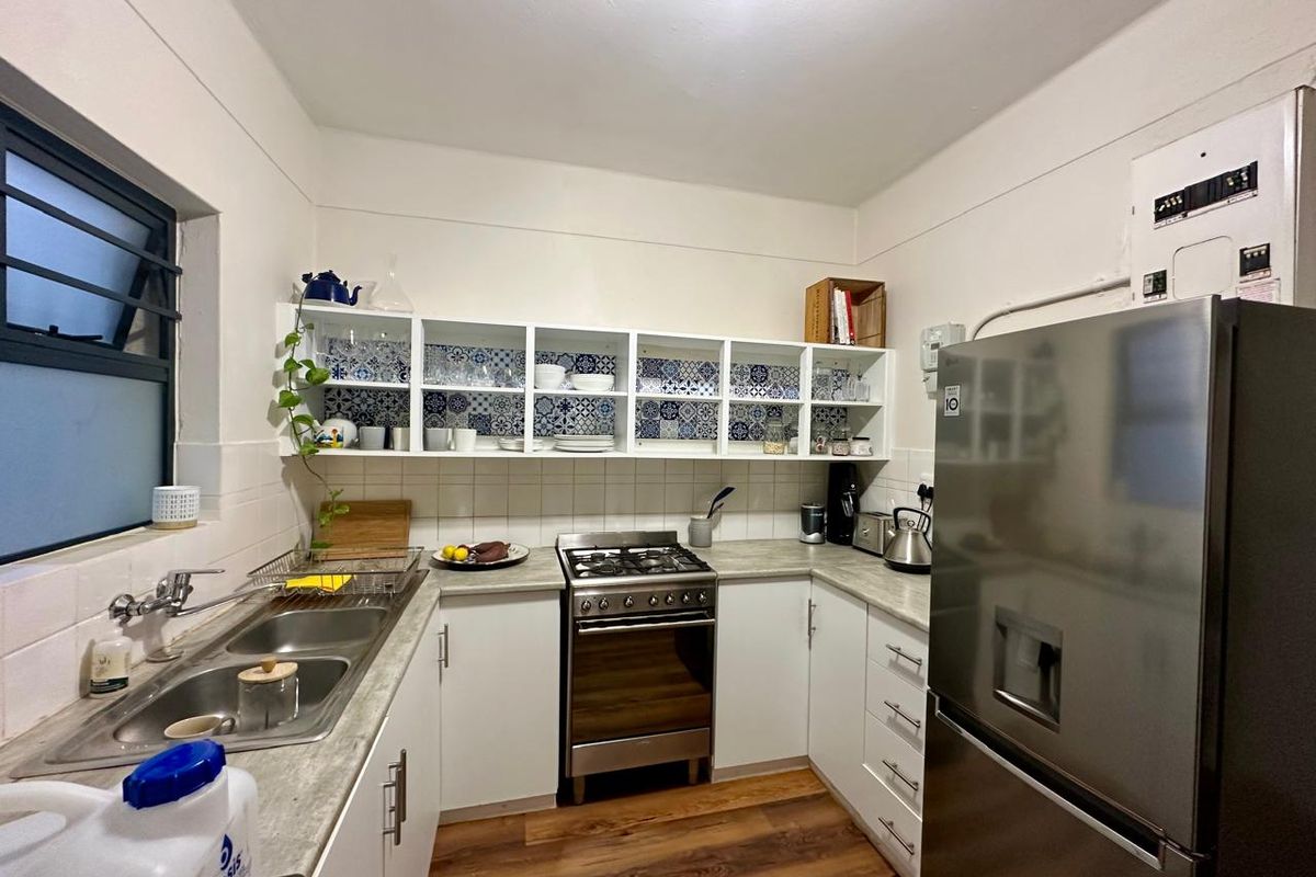 Compact kitchen featuring white cabinetry, patterned tile backsplash, stainless steel sink, and a built-in gas stove with oven.